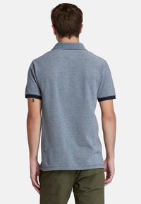 Lyhythihainen polo-paita vaaleansinisessä värissä, jonka kankaassa on tekstuuria ja tummansininen kaulus sekä hihojen reunat. Klassinen malli, takanäkymä.