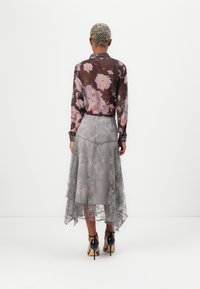 Sheer blomsterbluse med rosa og lilla blomster mønstre, parret med en grå blonde nederdel med lagdelt kant. Sorte højhælede sko.