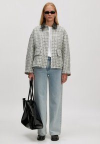 Grijze en witte stoffen blazer met een zwarte leren kraag, gecombineerd met lichtblauwe wijde jeans en een zwarte glanzende handtas.