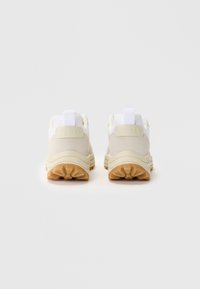 Sport shoes with a white mesh upper, beige suede accents, and a chunky cream sole. Rubber outsole with a textured grip pattern.