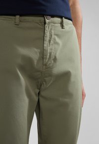 Chinos color caqui hechos de un tejido ligero, con cierre de cremallera, botón y bolsillos inclinados, con una textura suave y un ajuste entallado.