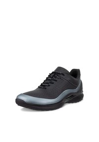 Chaussure de sport basse noire avec bordure réfléchissante grise, tige perforée, semelle rembourrée et lacets noirs sur fond blanc.