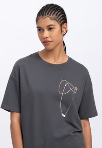 Grijze katoenen t-shirt met een ronde halslijn en korte mouwen. Bevat een minimalistisch abstract ontwerp in lichtrood en groen aan de linkerkant.