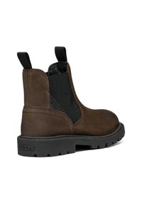 Botte Chelsea en cuir marron avec des panneaux élastiques noirs sur les côtés, des languettes de tirage et une épaisse semelle en caoutchouc noir marquée "GEOX" au talon.