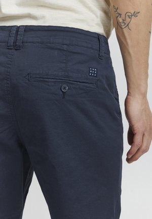Pantalons bleu marine en coton avec une texture lisse. Comprend une poche arrière avec un bouton et une petite étiquette logo.