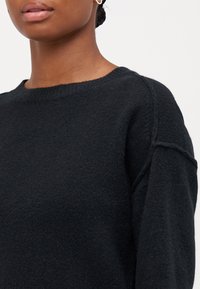 Sweater preto de malha com decote redondo, tecido texturado e mangas raglã, demonstrando uma aparência suave e confortável.