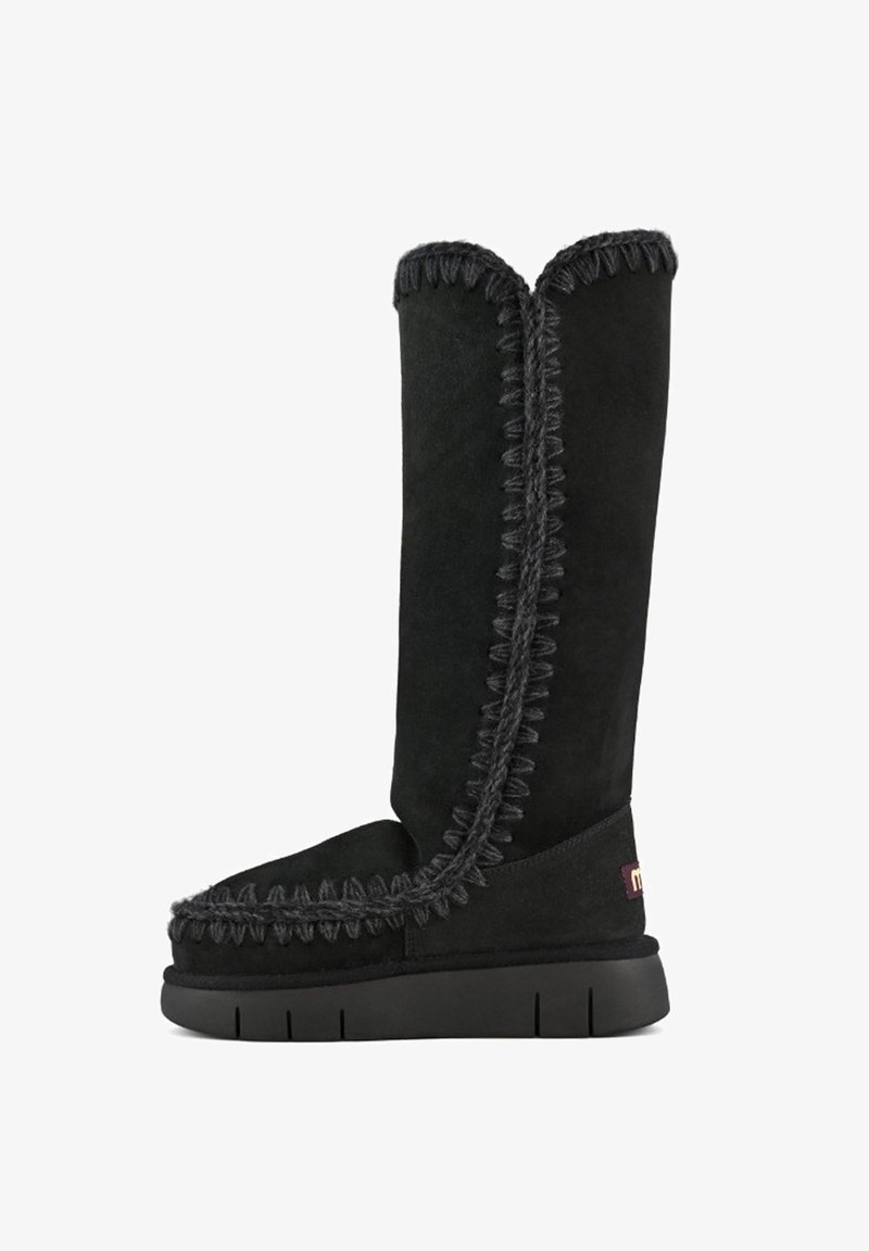 Stivale alto in suede nero con cuciture spesse a contrasto, finitura testurizzata e suola in gomma piatta. Presenta una patch con logo sul tallone.