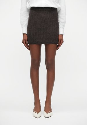 Korte, strakke bruine gebreide rok met een hoge tailleband. Gecombineerd met witte puntige hakken voor een schone, minimalistische uitstraling.