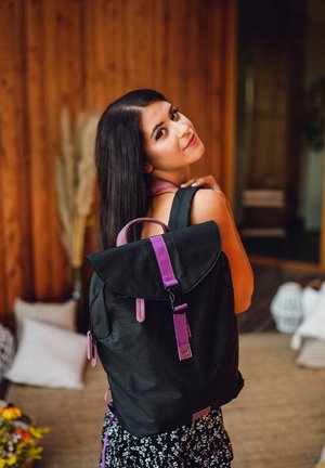Black backpack with a fold-over flap and purple straps. Features zipper pockets and a streamlined design. Textured fabric, casual look.
