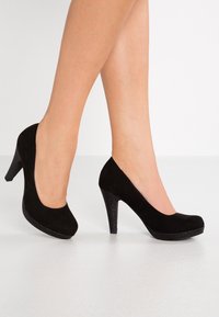 Chaussures à talons hauts en suede noir avec un bout rond, dotées d'un talon noir pailleté. Texture lisse avec un léger éclat sur le talon.