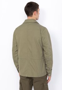 Oliven grøn, letvægtsjakke med klassisk krave, knaplukning ved h�åndleddene og en glat tekstur. Har et enkelt, udekoreret design.