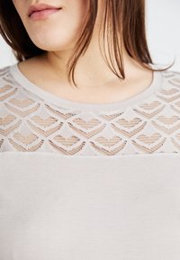 Ljusgrå stickad topp med en genomskinlig spetsok med hjärtmönster, kompletterad av en rundad halsringning och mjuk textur.