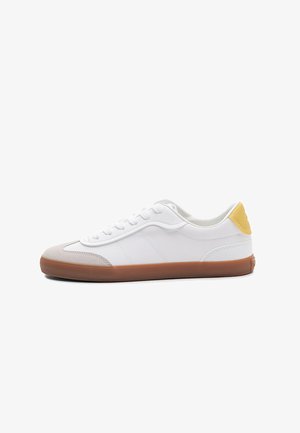 Sneaker bianca basse con suola in gomma, punta beige, lacci bianchi e linguetta posteriore gialla, mostrata di profilo su sfondo bianco.