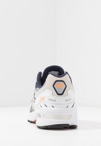 Vita och marinblå sportskor med nätövre del, orangea accenter och hexagonalt GEL-logotyp. Har dämpning och en gummisul.