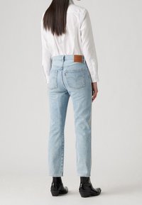 Světle modré denimové džíny se rovnými nohavicemi, vysokým pasem a kontrastním koženým štítkem na zadní straně. Nosit s bílou košlí a černými kotníkovými botami.