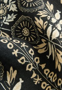 Tissu noir avec des motifs floraux et de feuilles blancs, présentant un tissage texturé. Les détails notables incluent des motifs circulaires et des designs complexes.