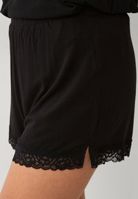 Zwarte satijnen shorts met een elastische tailleband, voorzien van delicate zwarte kanten randen aan de zoom en zijsplitten voor extra stijl en comfort.