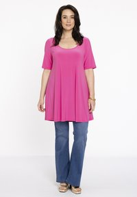 Lyserød, kortærmet tunika skjorte lavet af glat stof, der vidder ud ved taljen, parret med lyseblå kløftede jeans og gyldne platfrom sko.