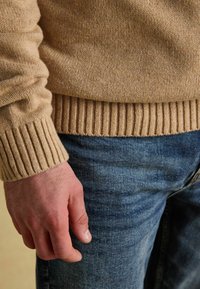 Beež ribaga kudumi, sobitatud varrukatega, koos siniste teksadega. Tuuakse esile tekstuur ja värvikontrast.