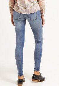 Vaqueros ajustados de mezclilla azul con un acabado deslavado, que cuentan con bolsillos traseros y un leve desgaste, combinados con zapatos negros.