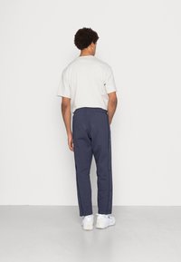 Marina joggingbyxor med en smal passform, med tryckknappar längs sidorna, tillsammans med en vit t-shirt och vita sneakers.