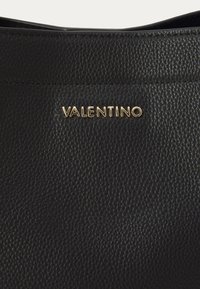Juodas odinis rankinukas su tekstūruota paviršiumi ir auksiniu "VALENTINO" logotipu. Paprastas, elegantiškas dizainas su išlenktu viršutiniu kraštu.