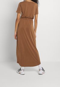 Robe maxi brune, longueur genou, avec des manches courtes et une taille élastique. Portée avec des chaussettes blanches et des chaussures de sport avec des accents noirs.