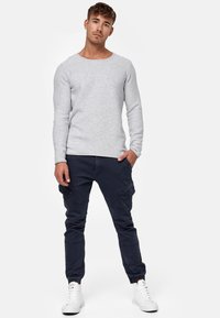 Suéter gris de manga larga tipo crewneck combinado con pantalones cargo azul marino. Los pantalones tienen bolsillos laterales y puños elásticos, completados con zapatillas blancas.
