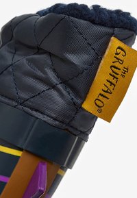 Gobelet en tissu gris isolé avec un dessus matelassé, étiquette jaune indiquant "Le Gruffalo," et rayures colorées près de la base en violet, rose et jaune.