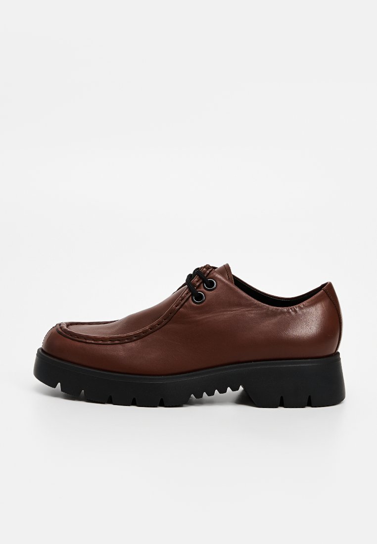 Bruine leren schoen met een afgeronde vorm, voorzien van een zwarte rubberen zool, vetersluiting en decoratieve stiksels langs de bovenrand.