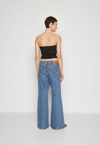 Top nero senza spalline con un design cropped abbinato a jeans a gamba larga blu con un lavaggio chiaro e cuciture classiche delle tasche posteriori.