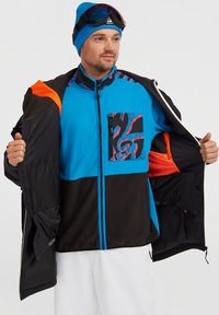 Giacca blu e nera con un accento arancione, dotata di una tasca con zip a motivo, di un interno foderato e di un design traspirante per le attività all'aperto.