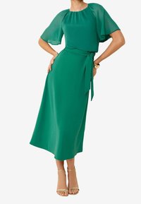 Vestido midi verde con mangas cortas y transparentes, cintura ajustada con un cinturón y una tela suave y fluida. Diseño sencillo, sin patrones.