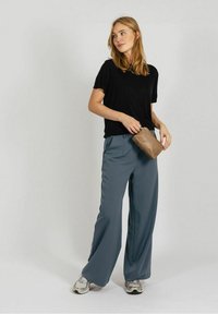 Črna kratka majica s kratkimi rokavi, ohlapna kroj, kombinirana s sivimi hlačami širokih hlačnic. Drži rjavo torbico. Srebrni športni copati dopolnjujejo obleko.