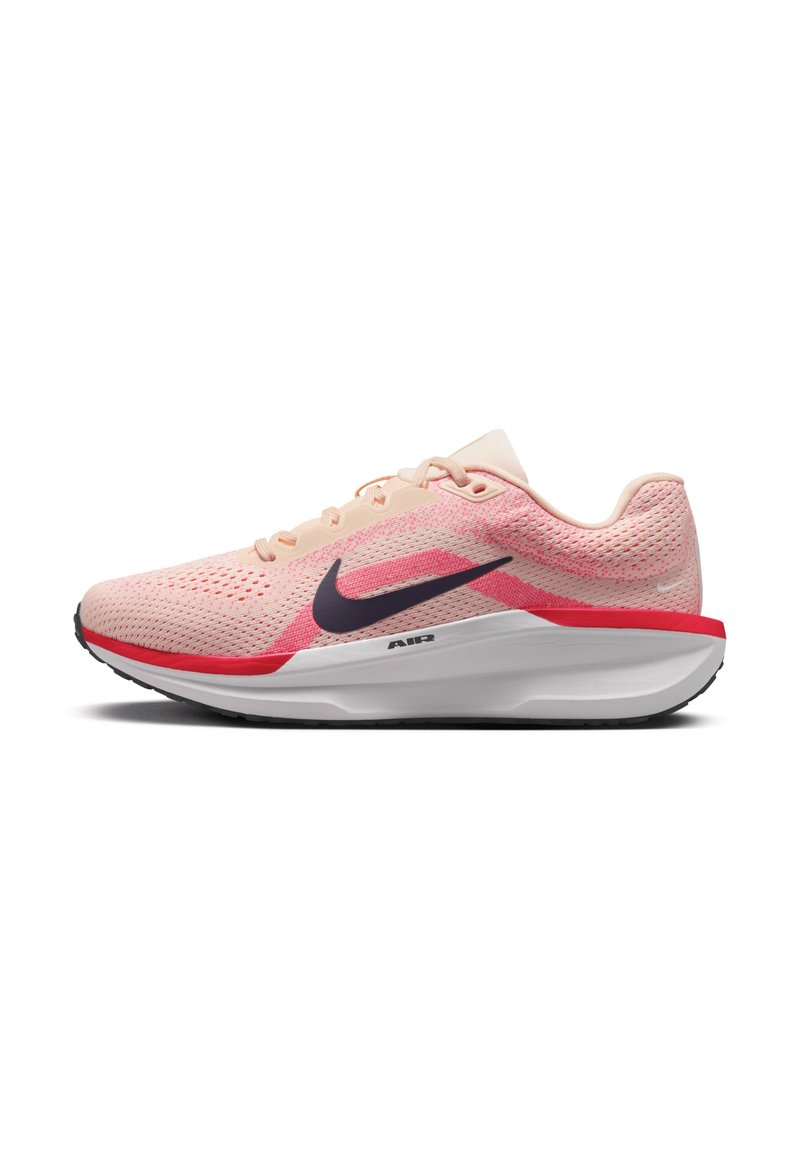 Chaussure de course Nike rose clair avec logo swoosh noir, accent rouge et semelle blanche rembourrée, vue de côté sur fond blanc.