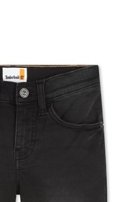 Jeans in denim nero con chiusura a bottone, tasche frontali e etichetta Timberland in vita. Caratterizzati da una texture sbiadita e dettagli a cucito.