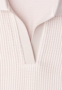 Tissu texturé rose clair avec motif gaufré et col en V doux avec une bordure côtelée lisse.
