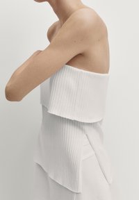 Top in cotone bianco a costine con design a strati e spalle scoperte. Presenta uno strato superiore testurizzato e fessure ai lati per facilitare i movimenti.