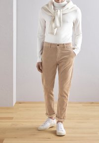 Pantalon en velours côtelé beige clair à coupe droite, avec une texture subtile et des revers roulés, associé à un col roulé blanc  à manches longues et des baskets blanches.