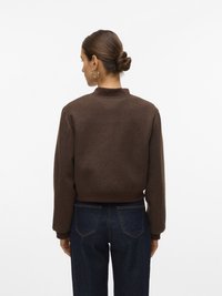 Sweatshirt brun court avec un col montant, des poignets côtelés et une taille côtelée, associé à un jean droit bleu foncé.