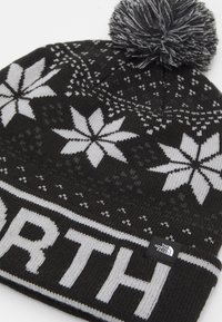 Musta kudottu pipo, jossa on harmaita lumihiutaleita, pom-pom päässä ja "NORTH" paksuilla kirjaimilla. Brändin etiketti näkyvissä viehättävässä reunassa.