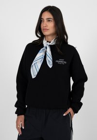 Czarna bluza z napisem "PROHIBITED Racing Club", zestawiona z niebieskim jedwabnym szalikiem w wzory. Charakteryzuje się luźnym krojem i miękką fakturą.