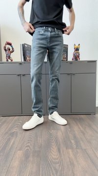 Jeans ajustados de color azul claro con un aspecto deslavado, combinados con zapatillas blancas. El fondo incluye armarios grises y figuras decorativas coloridas.