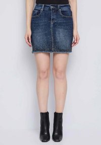 Minigonna di jeans blu scuro con tasche frontali, orlo sfrangiato e impreziosita da piccoli strass. Abbinata a stivaletti neri alla caviglia.