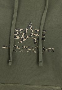 Olivno zeleni hoodie z teksturiranim vrvico, zvezdnim logotipom v leopardjem vzorcu in črnim besedilom. Mehka tkanina z gladkim koncem.