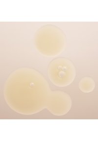 Blassgelbe Öltropfen in verschiedenen Größen, die auf einem hellen Hintergrund verstreut sind, mit glatten Oberflächen und einer glänzenden Textur.