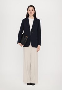 Marineblauwe getailleerde blazer met één knoop, witte crew neck shirt, beige wijde broek, en een zwarte leren handtas met gouden hardware.