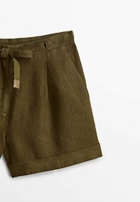 Short en lin vert olive avec ceinture en tissu, poches latérales, plis et revers sur fond blanc.
