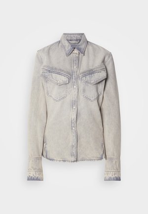 Light-wash denim shirt with a pointed collar, two chest pockets, and button closure. Features contrasting stitching and frayed hem.