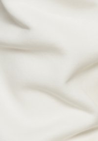 Weißer Stoff mit glatter Textur, sanft zerknittert und zeigt feine Webdetails. Das Licht spiegelt sich sanft von der Oberfläche wider.